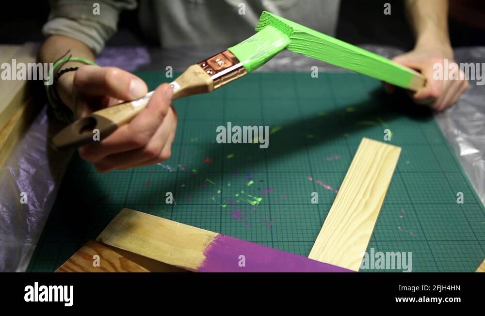 Girl is painting a wood stick with light green varnish in the studio