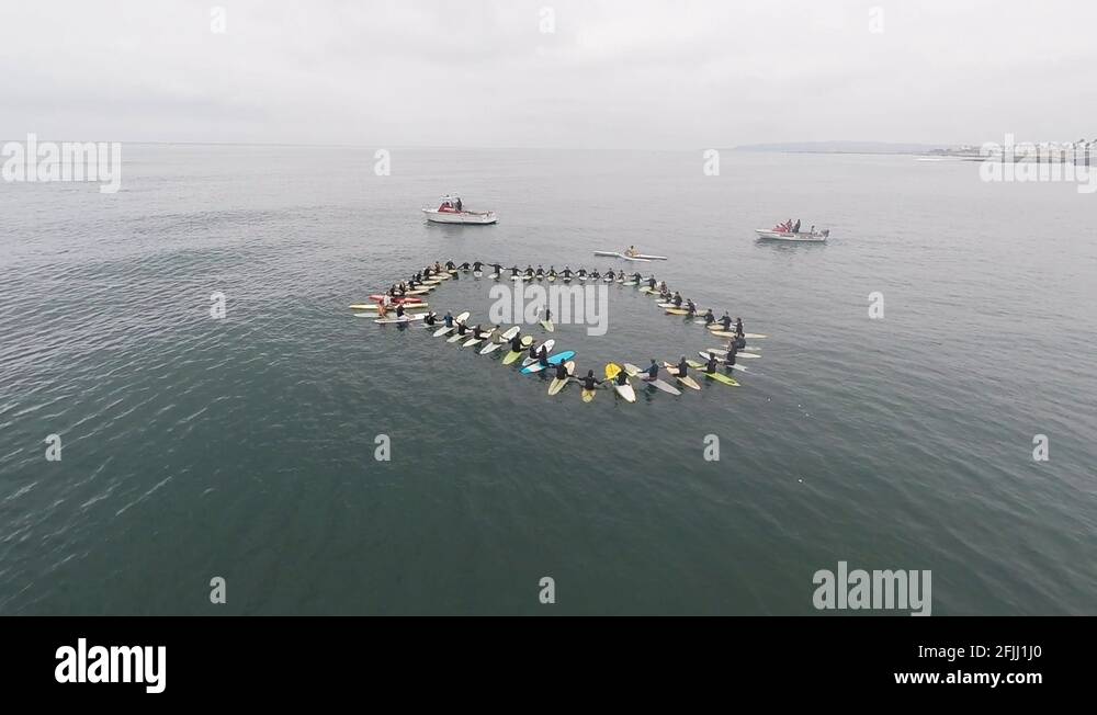 Aerial pull back shot away from surfers sat holding hands in circle Stock Video Footage Alamy