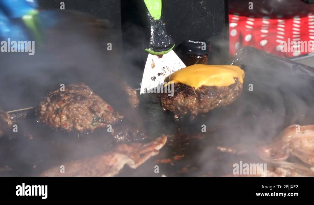 Chef cooking burgers on a griddle pan at a street food market Stock