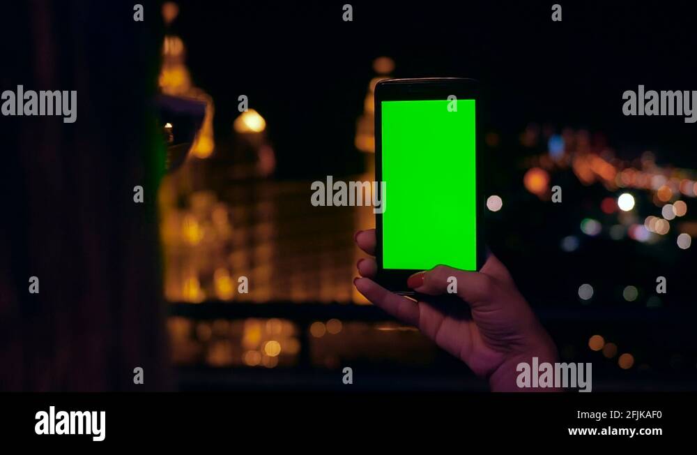 Close up woman hand holding phone with green screen blurred night city ...