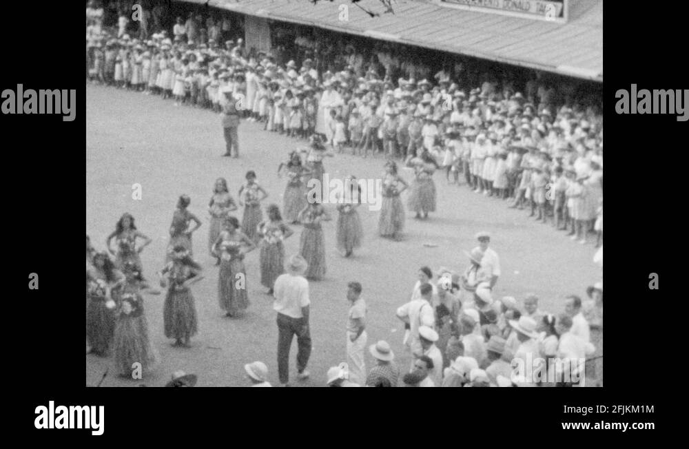 1940s Dense crowd watches women dance in grass skirts, wave hands
