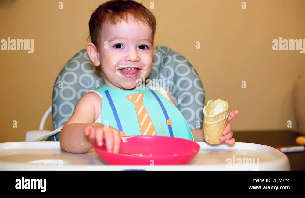 Baby in the breastplate eats ice cream in a waffle cup, the face of the child is Stock Video