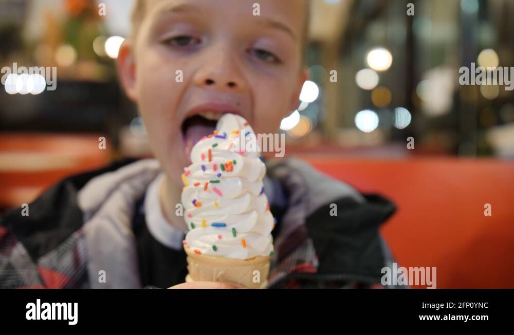 Young boy in a restaurant licks vanilla ice cream cone with sprinkles ...