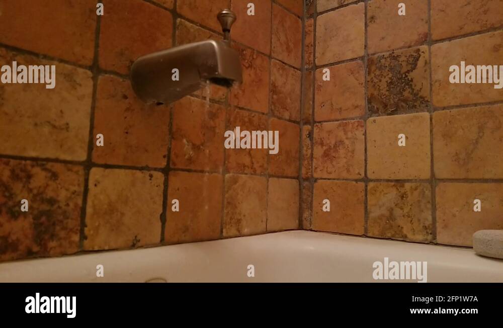 Faucet water trickles into bathtub, foreground to a golden background