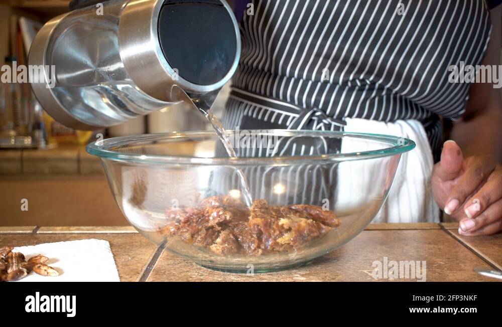 Woman pouring boiling water on dried dates in glass bowl, Close Up