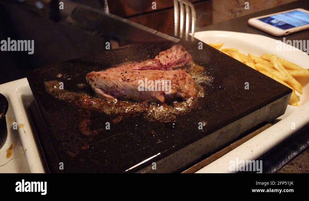 Girl Cuts A Juicy Piece Of Steak With A Knife On A Hot Rock Plate At