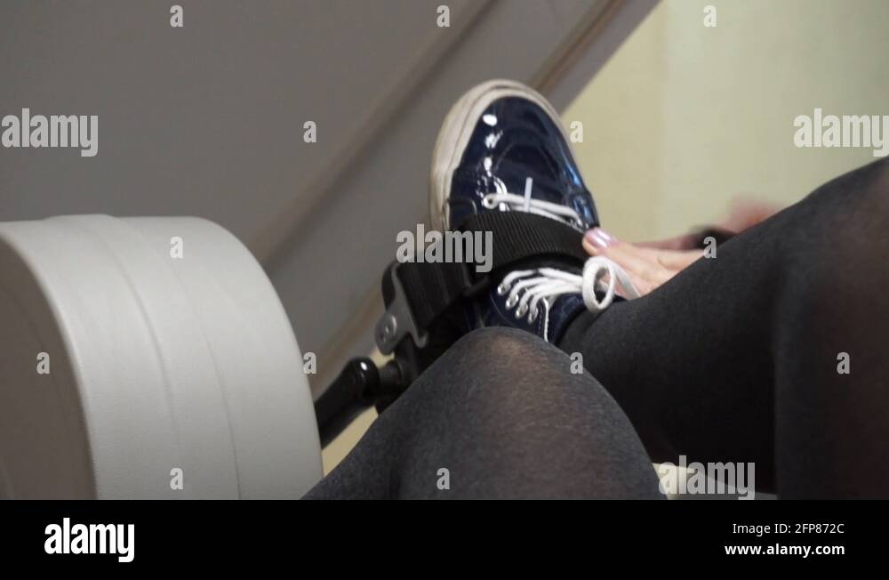 Close Up Woman Strapping Her Feet Into A Recumbent Exercise Bike Stock