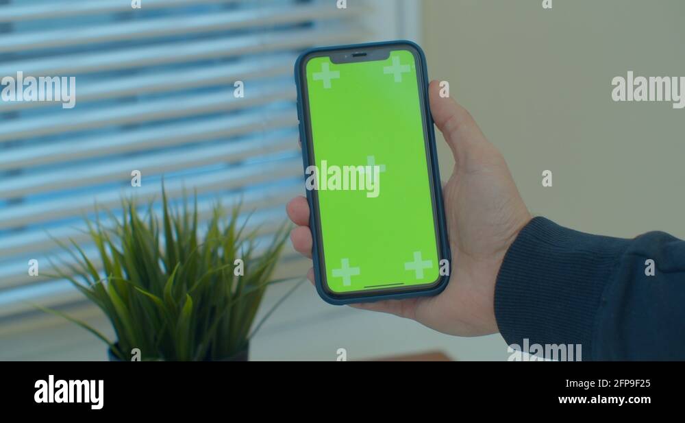 Close up of a man hand holding a mobile telephone with a vertical green ...