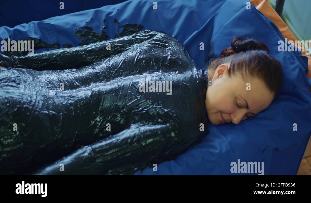 Relaxed young woman lying on spa bed for body massage using mud Stock