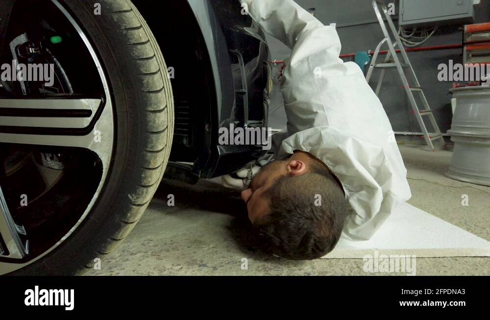 Repair man lying on ground and attaching new bumper on sport car in