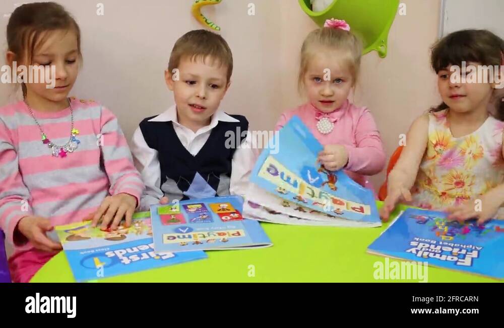Four children sit at the table and open textbooks in English Stock