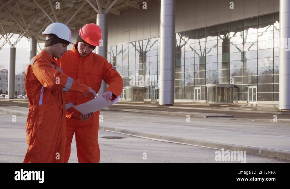 Two construction workers in orange uniform and hardhats looking over ...