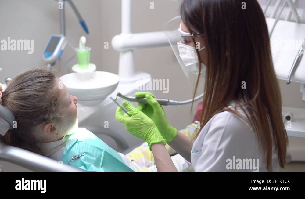 Female dentist drilling tooth of cute little girl at the dentist