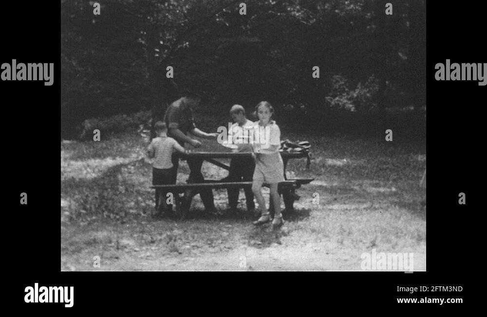 1940s Family at picnic table, girl brings hot dog to fire / Boy and