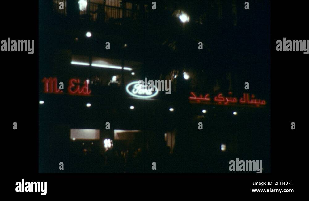 1950s: Lit Up Ford Sign on Building at Night. Car Driving through ...