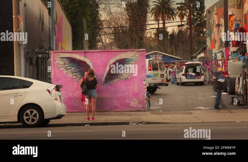 People take photos in front of pink wall big painted graffiti wings