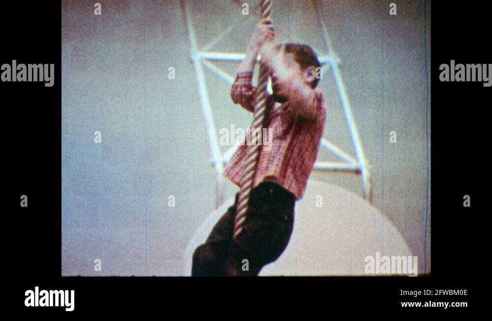 1960s: Young boy in jeans and plaid shirt shimmies up a rope Stock ...