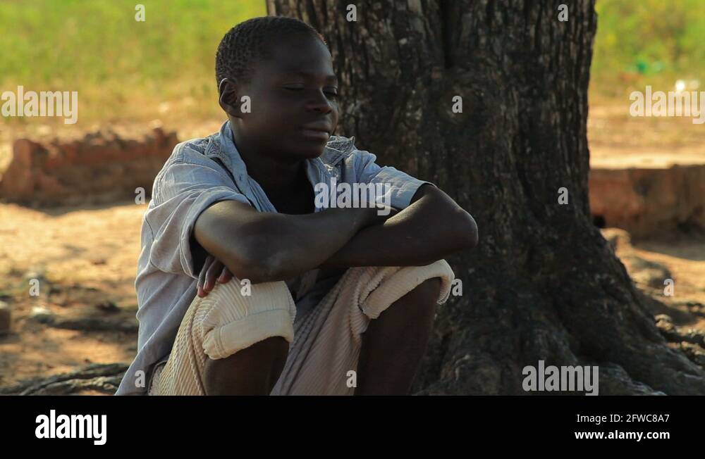 Kenyan boy sitting under a tree, thinking Stock Video Footage - Alamy