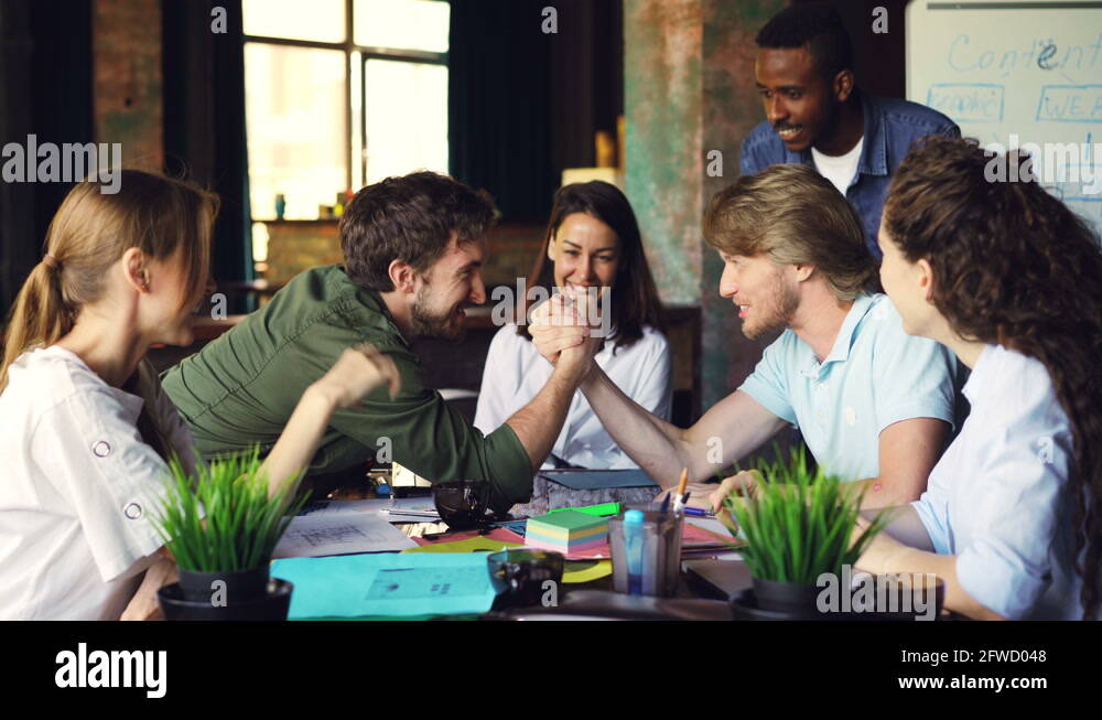 Two young men are competing in arm wrestling during break at work while
