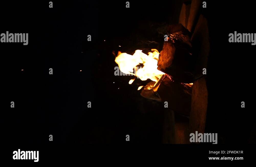 VERTICAL, orange flames flickering and embers glowing on outdoor fire