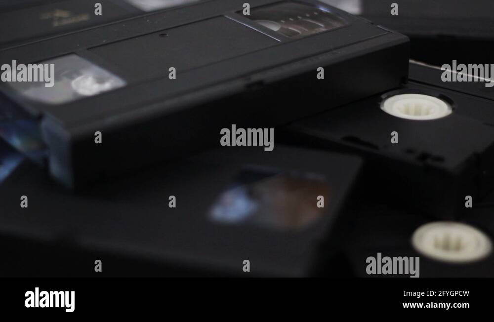 Take a vhs cassette tape from a stack of tapes and put it again on