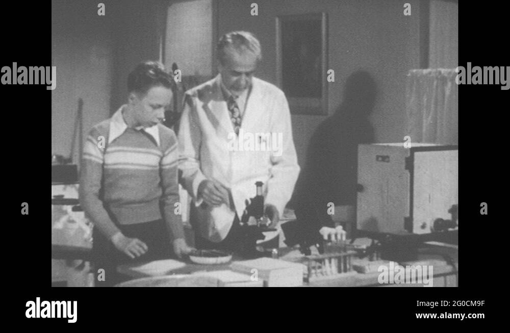 1950s United States Doctor And Boy Look At Germs Under Microscope On