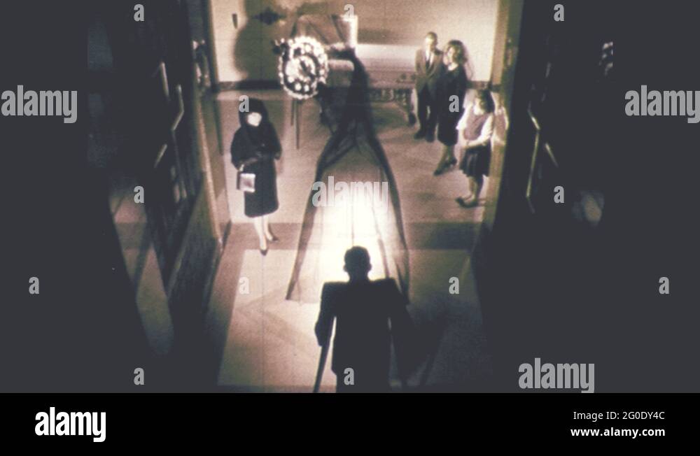 1960s Man with amputated leg walks on crutches towards coffin at a