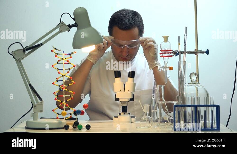 Man taking off eyeglasses looking at microscope in chemistry laboratory