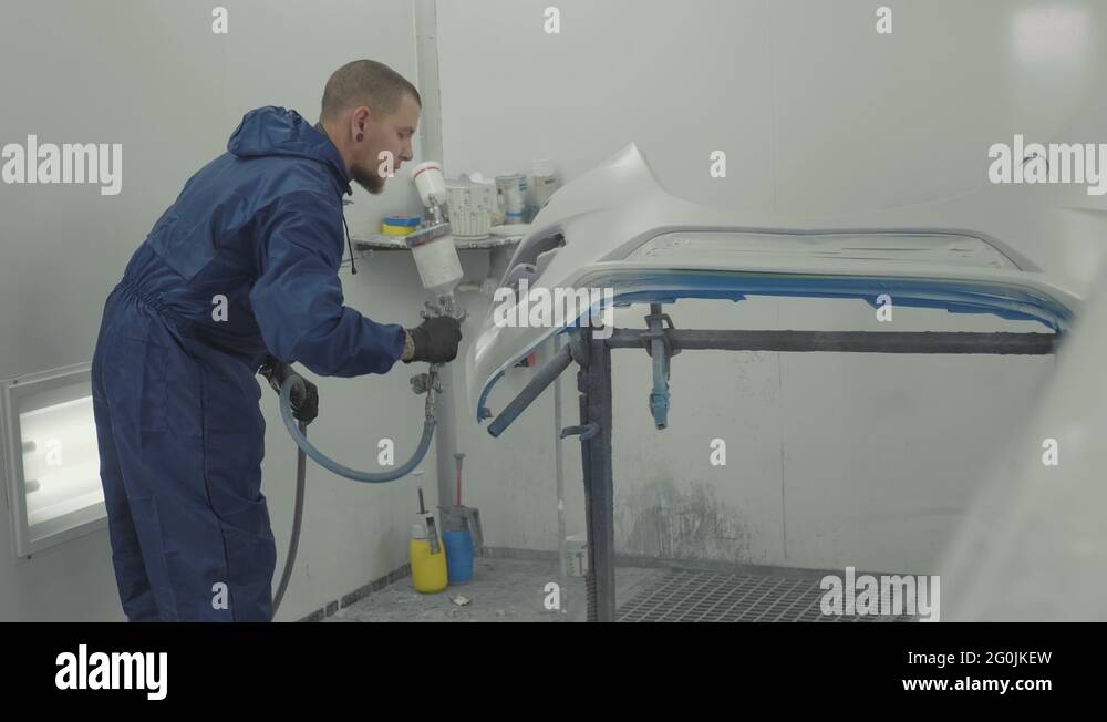 Auto painter spraying white paint on car front bumper in special booth