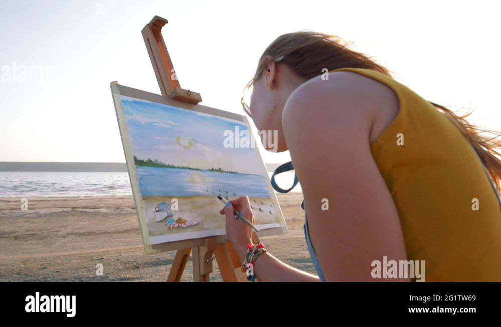 Young woman artist painting landscape in the open air on the beach ...