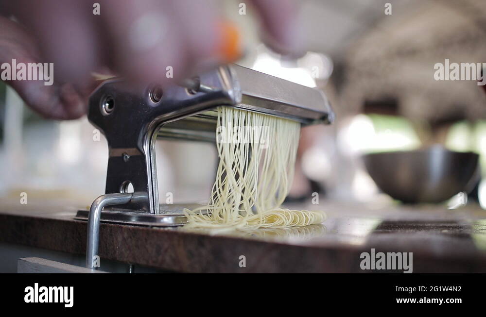 Chef's hands use a pasta cutting machine. Fresh spaghetti pasta coming