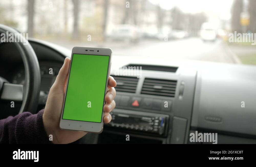 A hand holding a smartphone with green blank screen in the car for ...