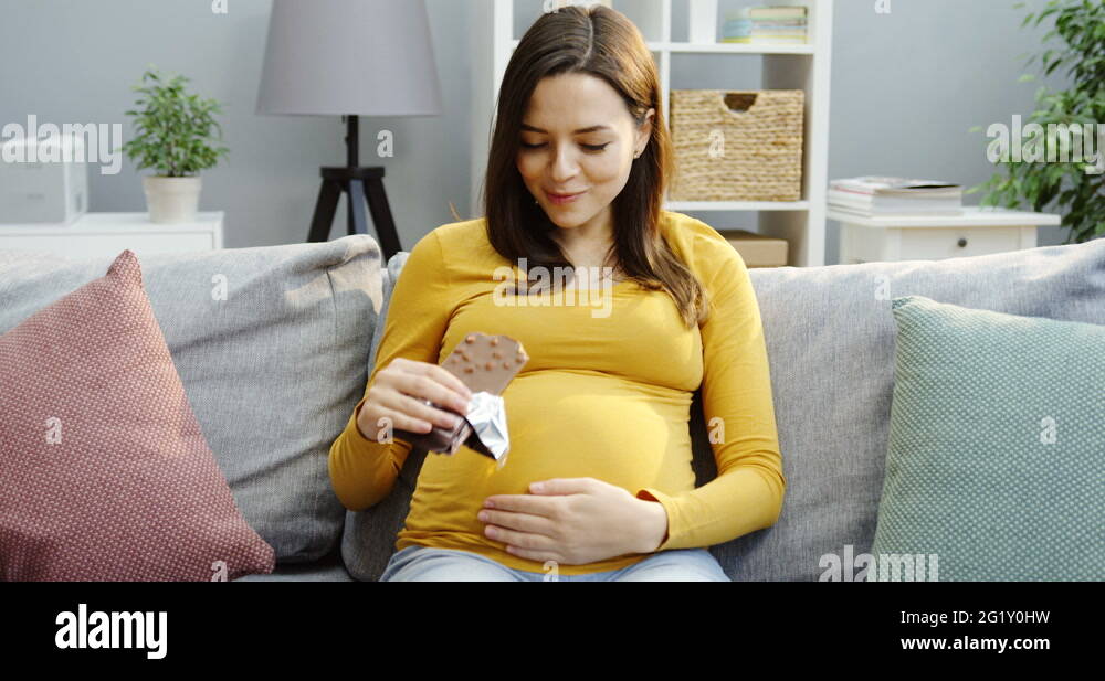 Beautiful pregnant woman eating a chocolate bar with nuts while sitting