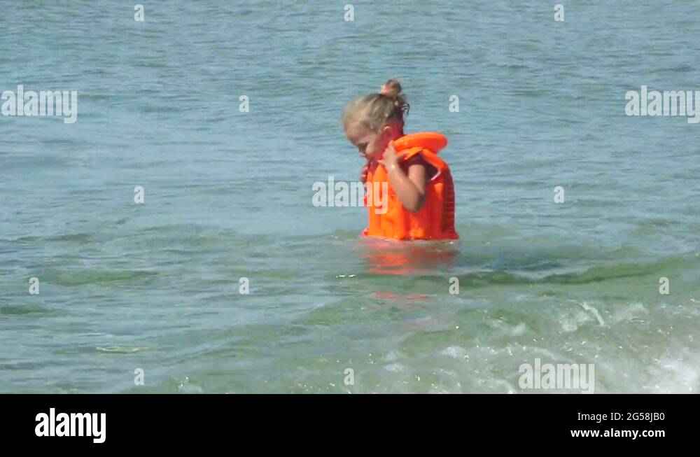 Little girl in inflatable life jacket learning to swim on beach