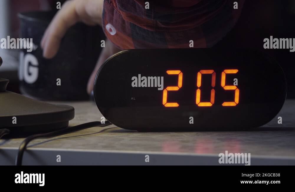 Black rectangular shaped electronic digital clock shows time in orange