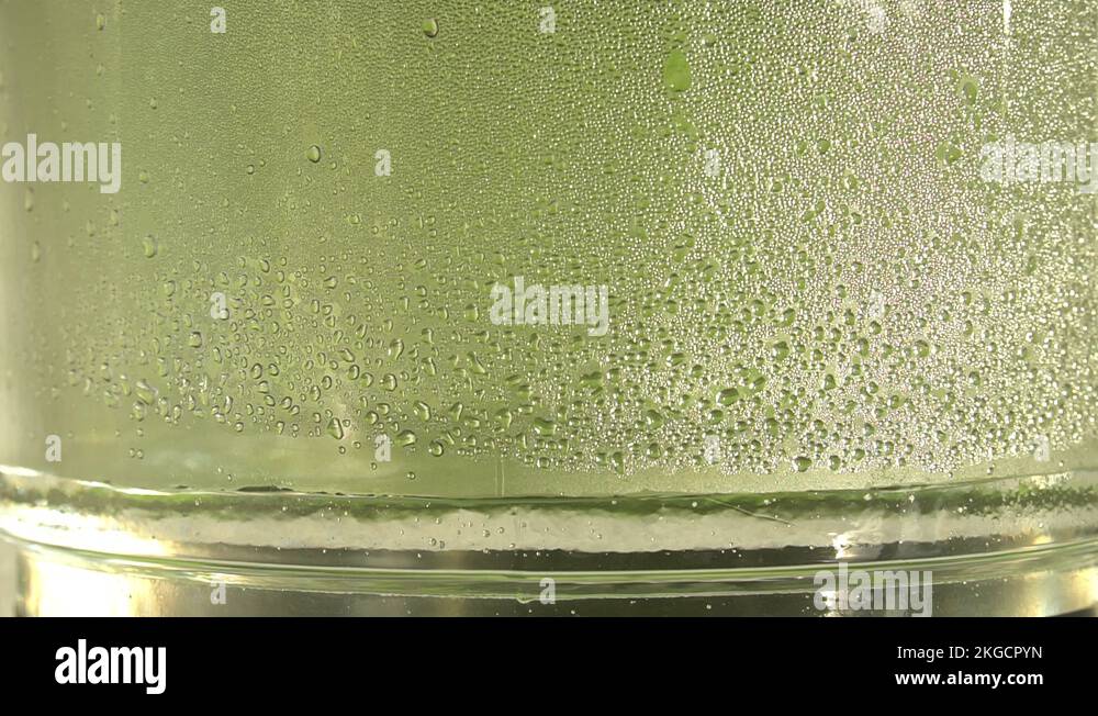 Drops of pure water or alcohol drip inside a glass jar, on green back