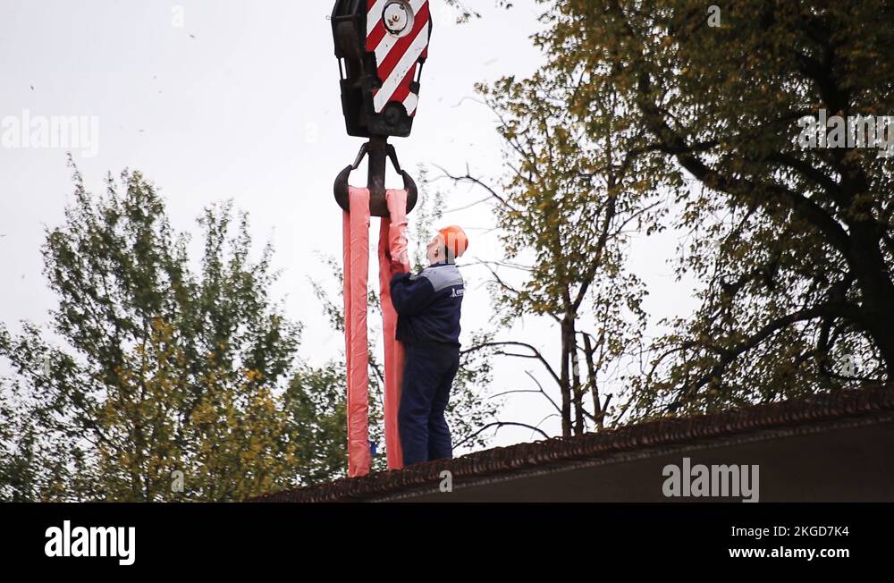 Workman in uniform and orange helmet fixates pink hoses on crane hook