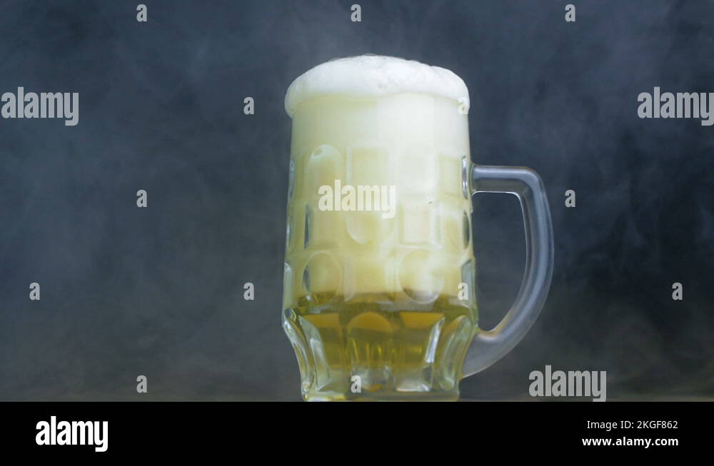 foam flows out of the glass of pilsener or lager beer in smoke in slow