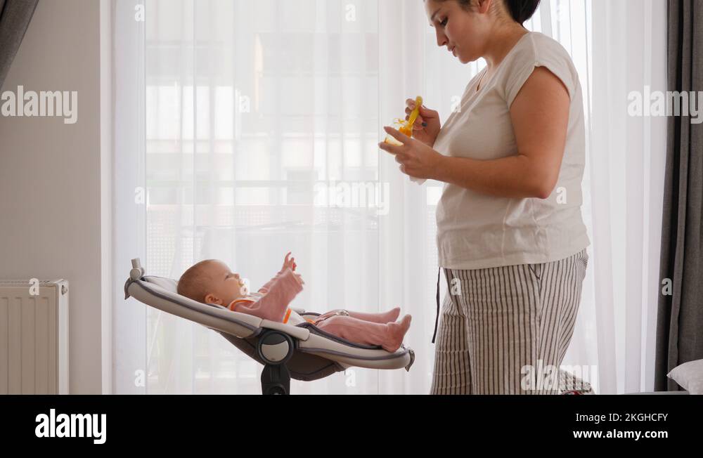 22 Mother leans to the child that lie in baby swing and feed with first