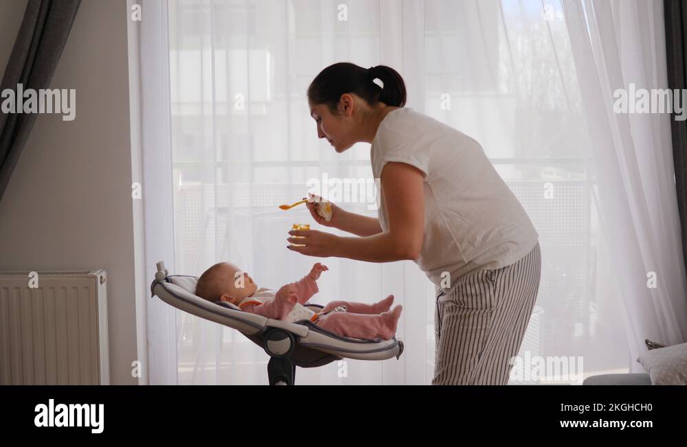 29 Mother leans to the child that lie in baby swing and feed with first