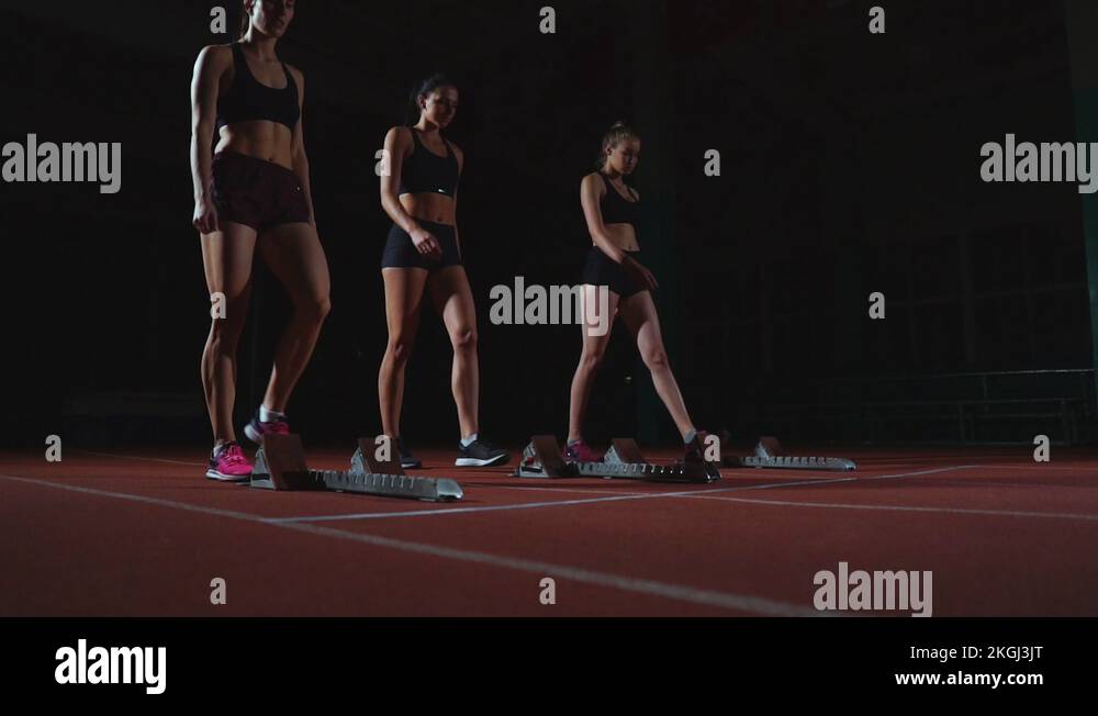 Female runners at athletics track crouching at the starting blocks ...