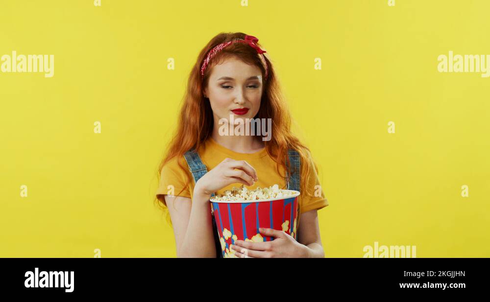 Beautiful young woman with long red hair holding a big popcorn and