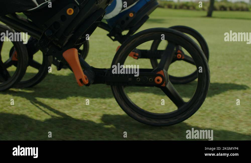 Golfers. Walking up fairway pushing carts. Wheel and fairway cu A Stock