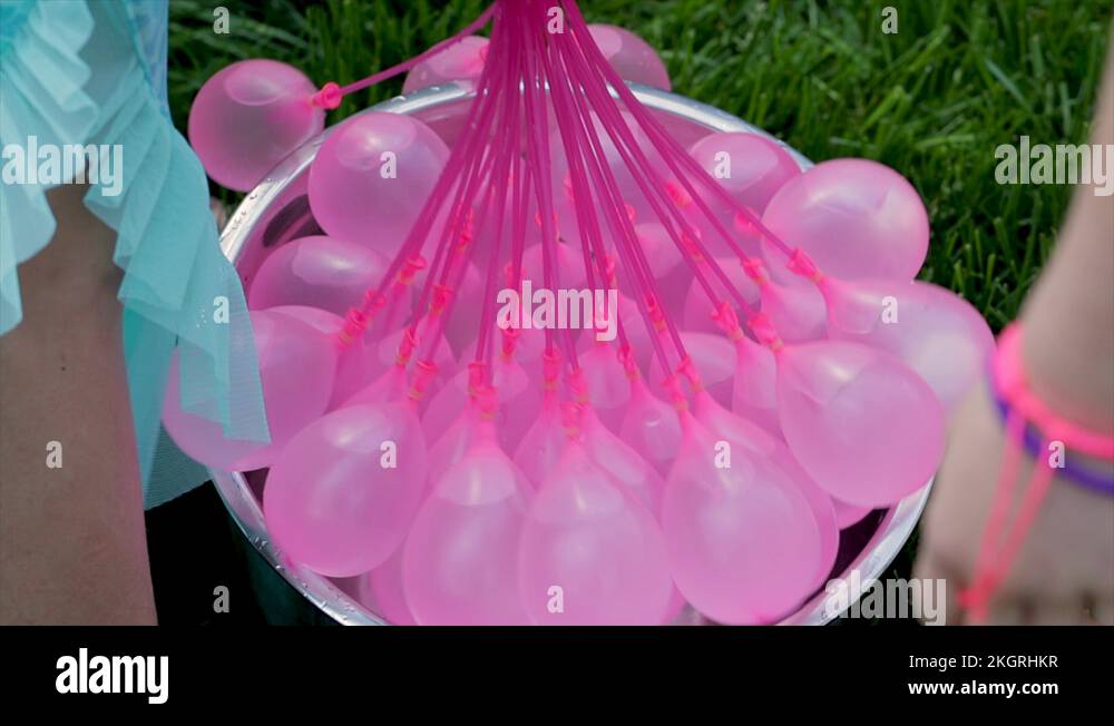 Children playing with pink water balloons. Girls using a water to hose