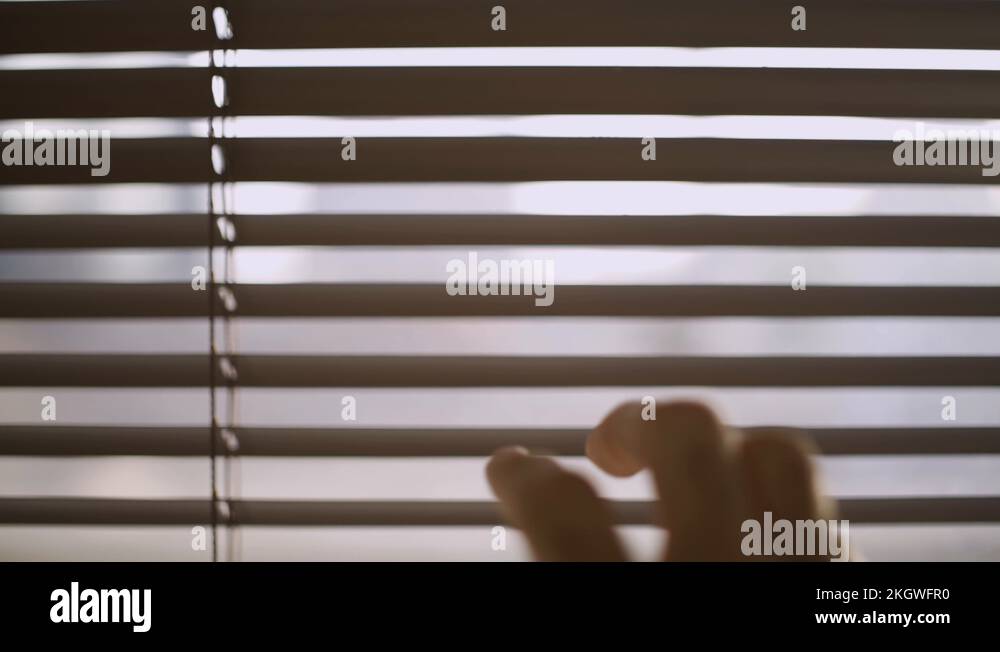Close up of a hand reaching and opening a crack in the window blinds