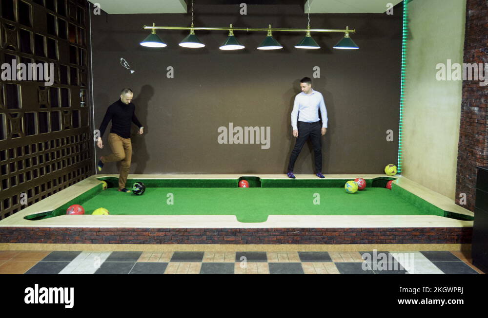 Two men playing billiards, hitting balls into holes on a floor billiard