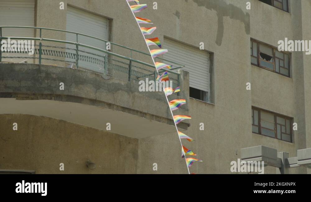 A strip of Gay Pride flags hang on side of a building flags blow in