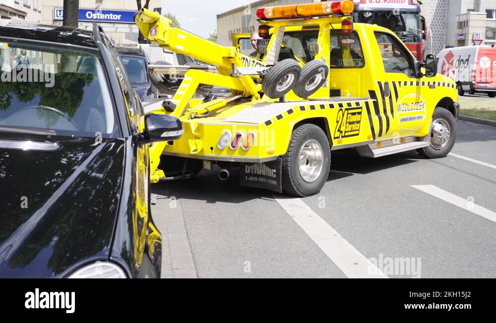 Tow service truck with flashing lights lifting wrongly parked car Stock