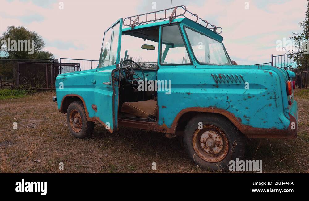 A bizarre old retro aquacolored car on a meadow with one door opened