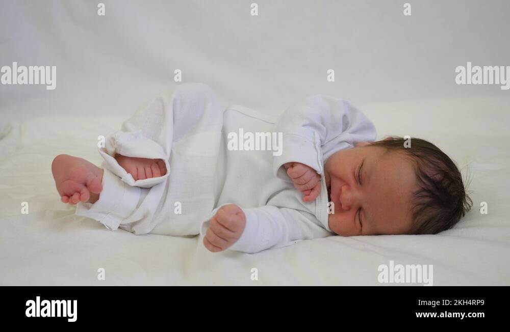 Newborn baby child on bed moves tiny hands and legs, open mouth Stock